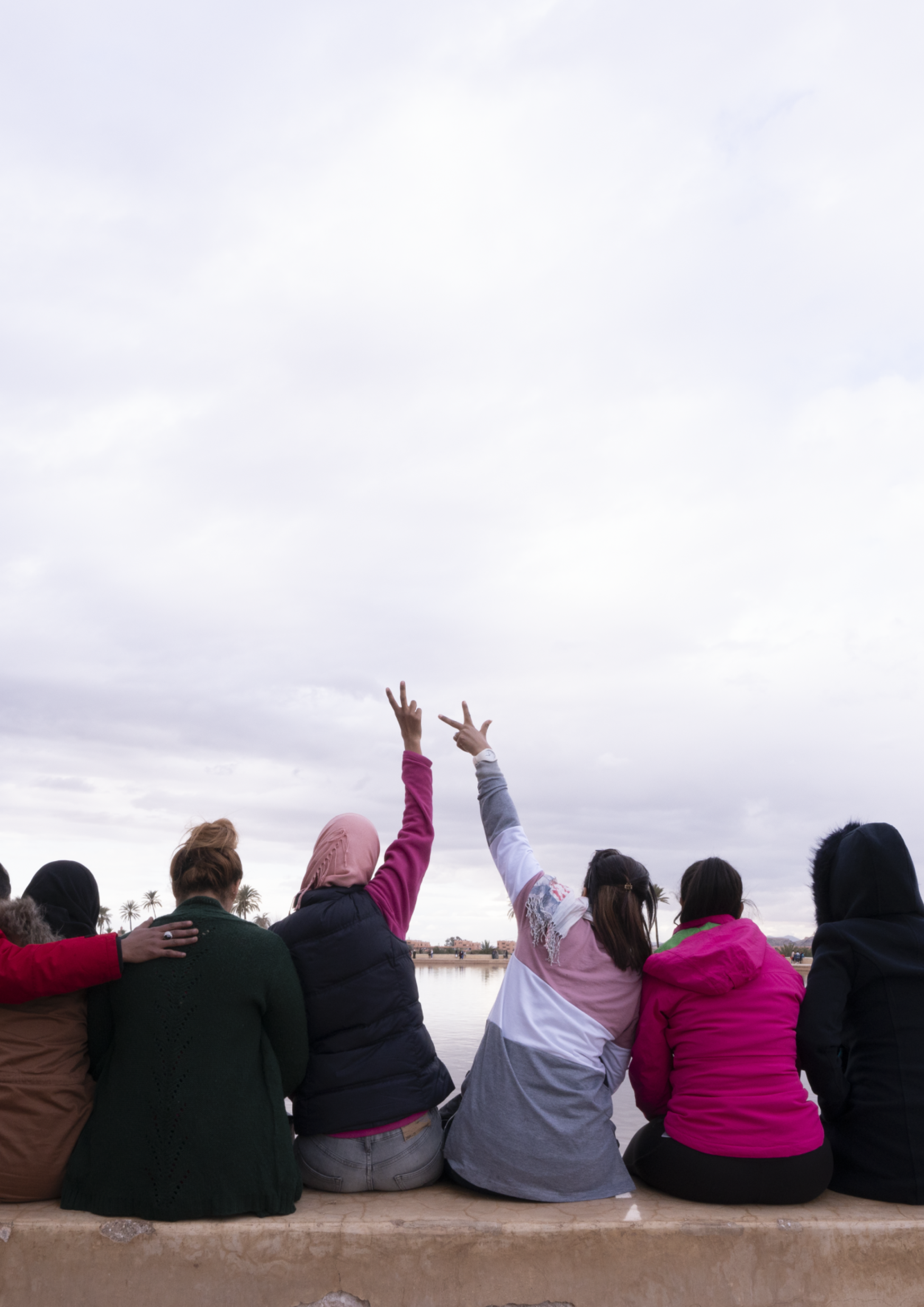 Frauen und Teilnehmerinnen des Projekts von Frieda sitzen vor einem Gewässer und schauen in die Ferne.