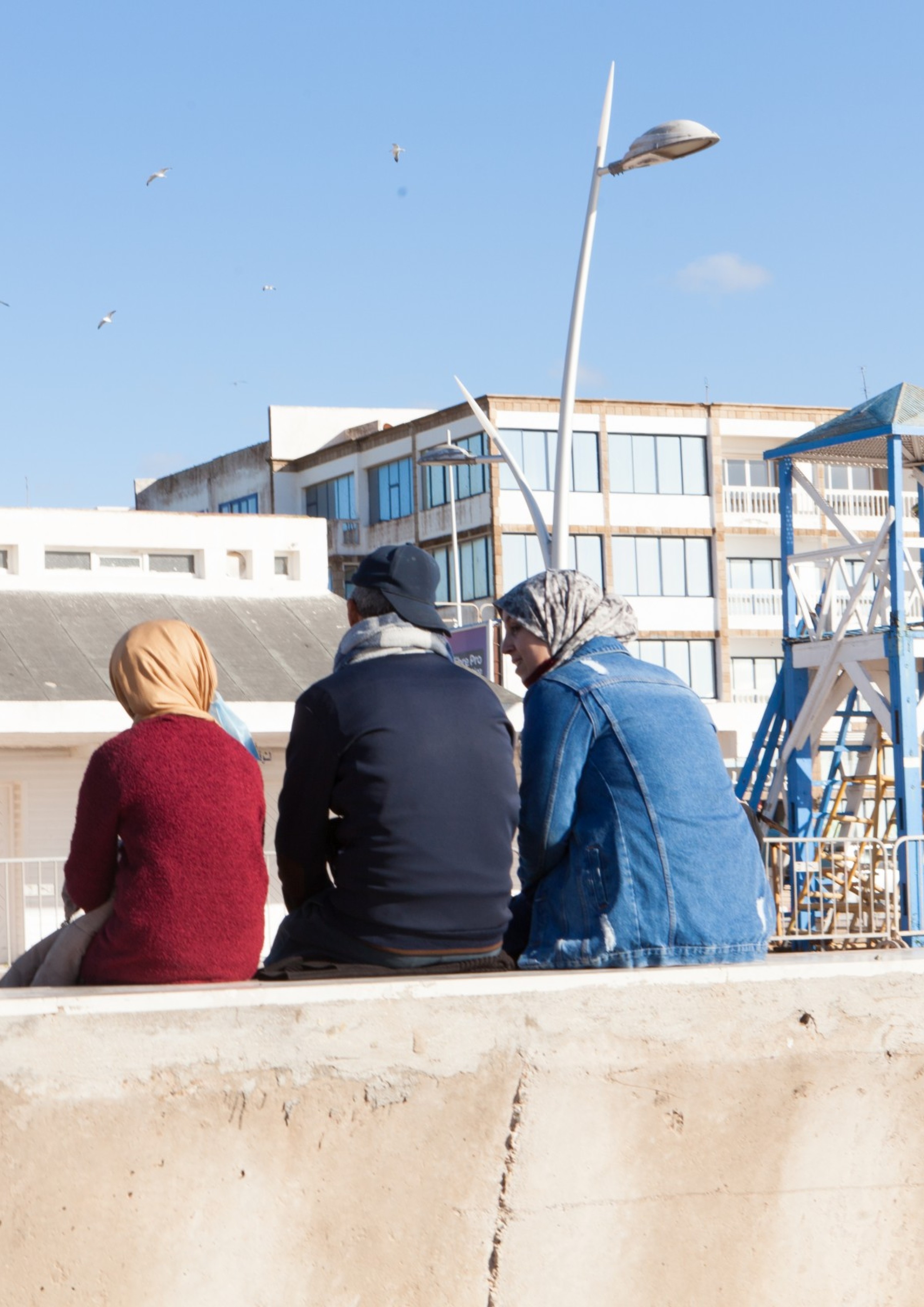Zwei Frauen und ein Mann sitzen in Marokko auf einer Mauer.