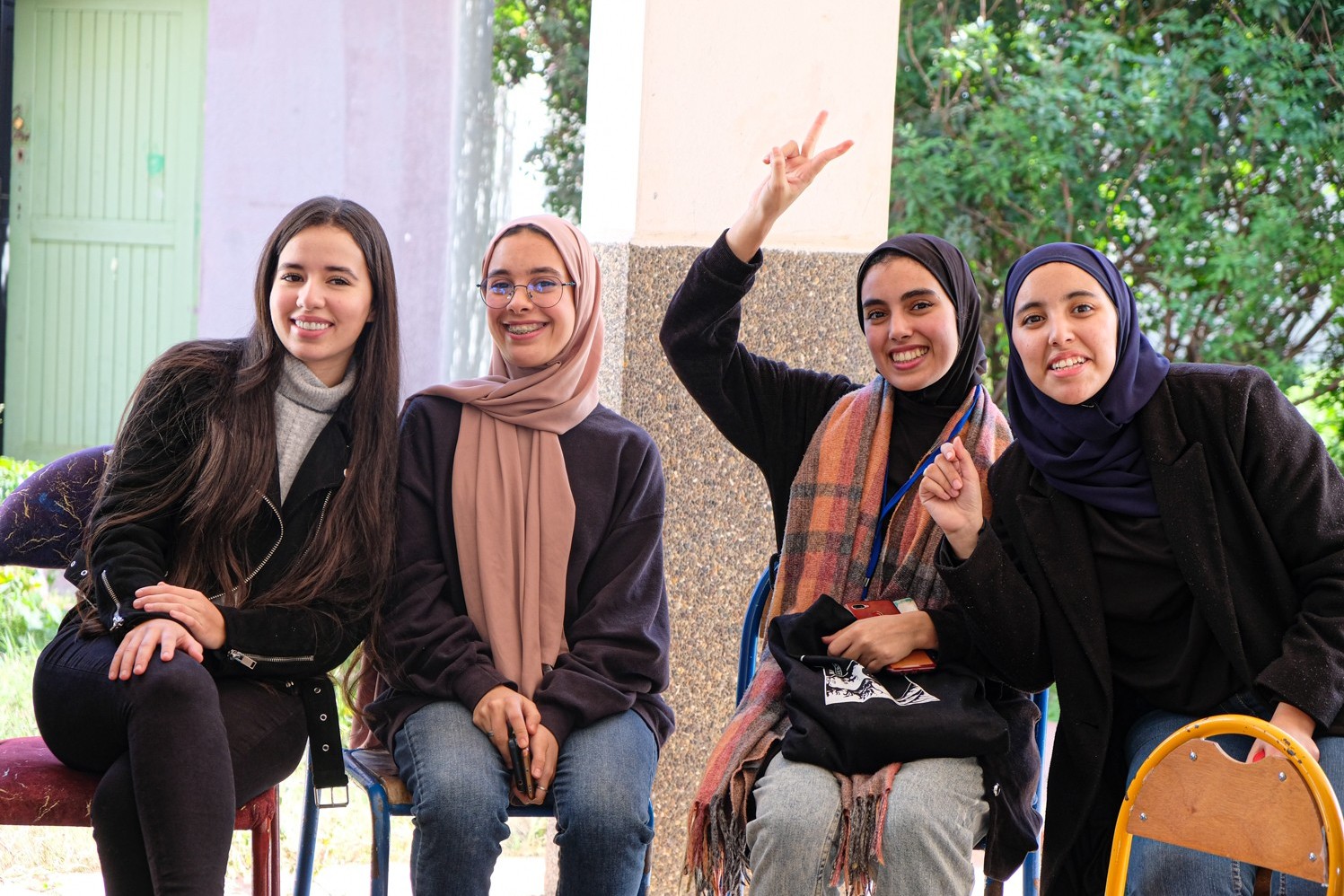 Vier marokkanische Frauen sitzen lachend auf Stühlen und zeigen das Peace-Zeichen