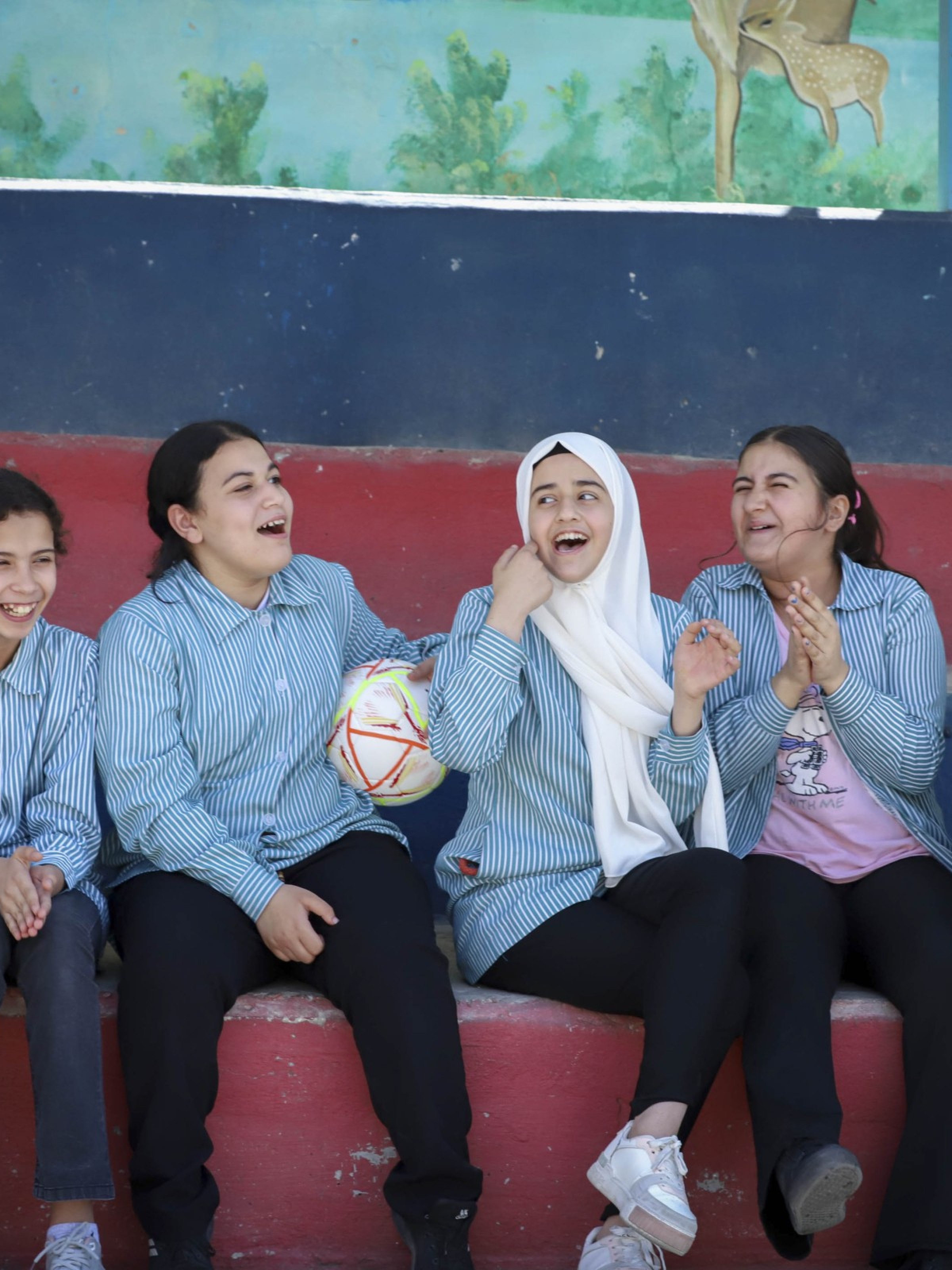 Junge Frauen in der Westbank sitzen an einem Spielfeldrand mit einem Fussball und lachen
