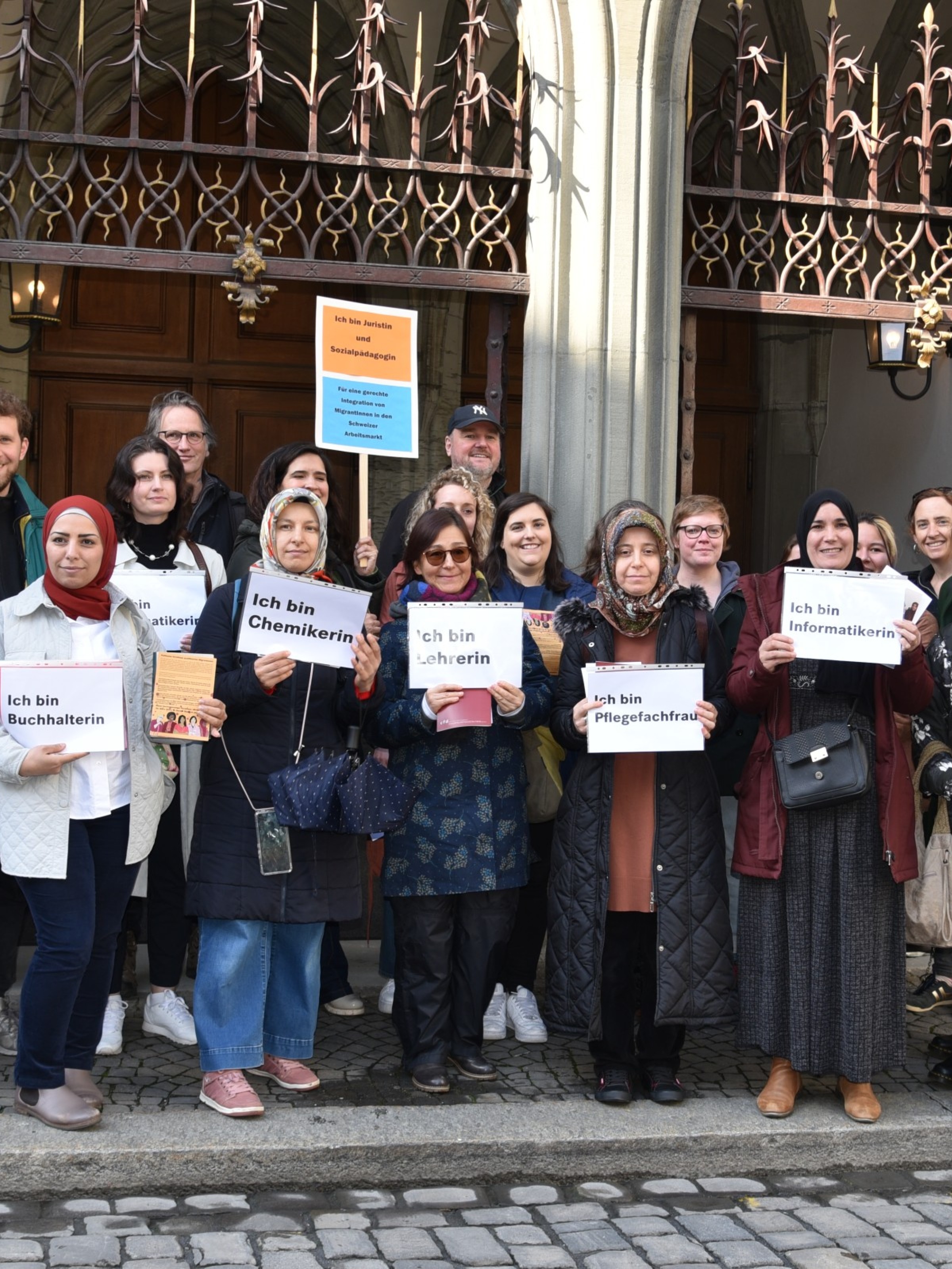 Frauen mit Migrationshintergrund halten Schilder mit Berufsbezeichnungen während einer Demo in Bern
