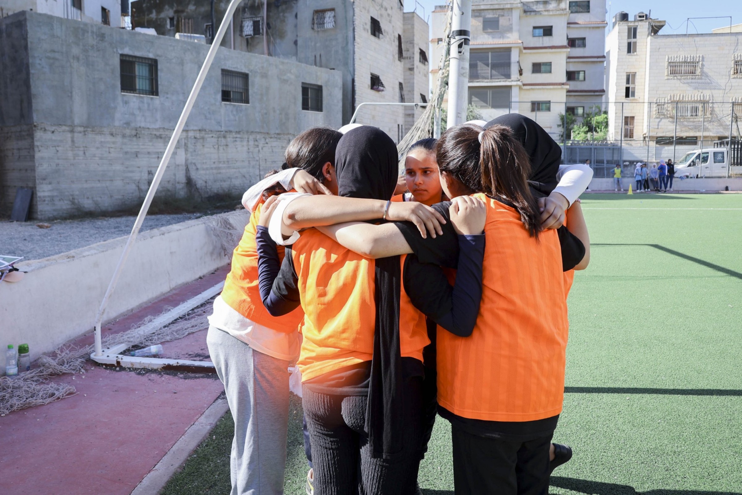 Junge Mädchen mit orangen Trikots stehen in einem Kreis und halten sich fest
