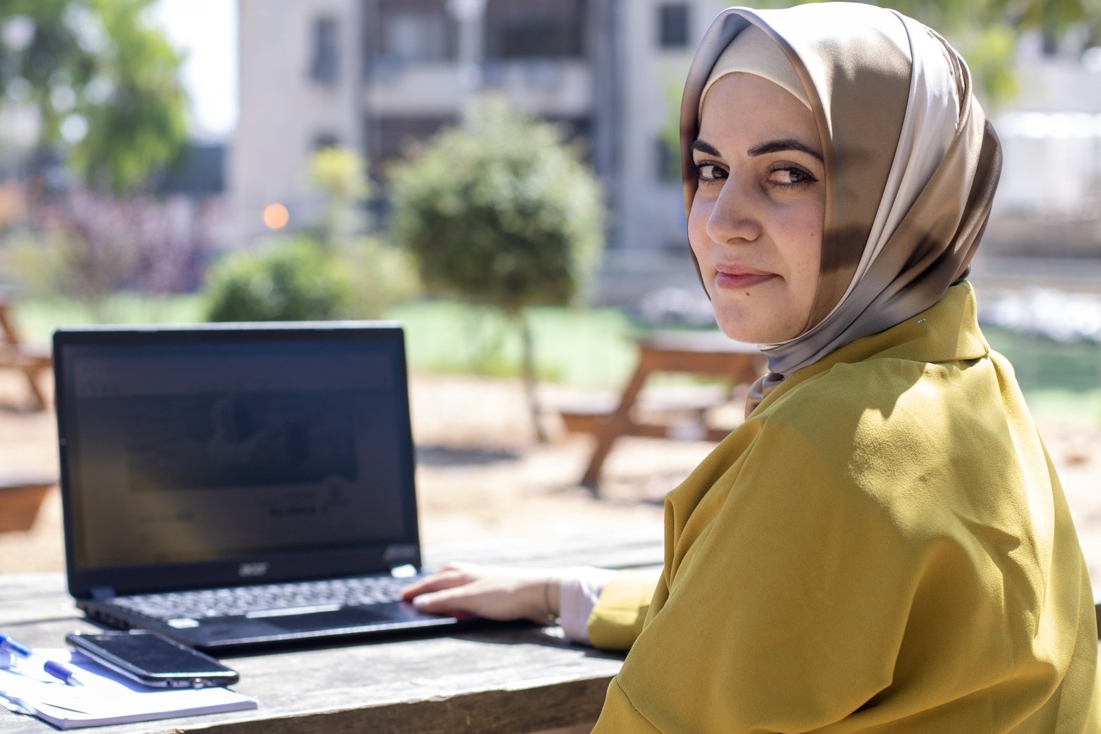 Junge Frau mit Kopftuch sitzt draussen mit einem Laptop