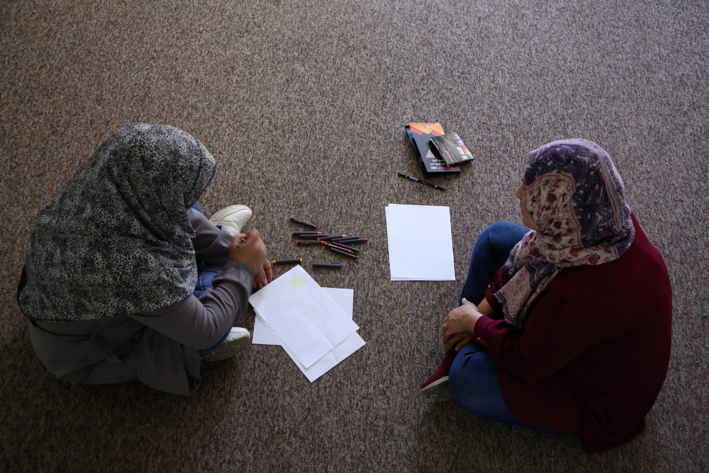 Frauenen in Palästina sitzen auf dem Boden mit Blätter und Stifte vor ihnen.