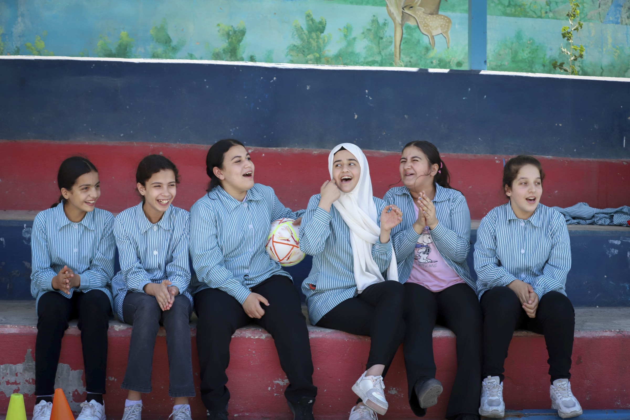Mädchen aus Palästina sitzen auf der Wartebank beim Fussballspiel und lachen.