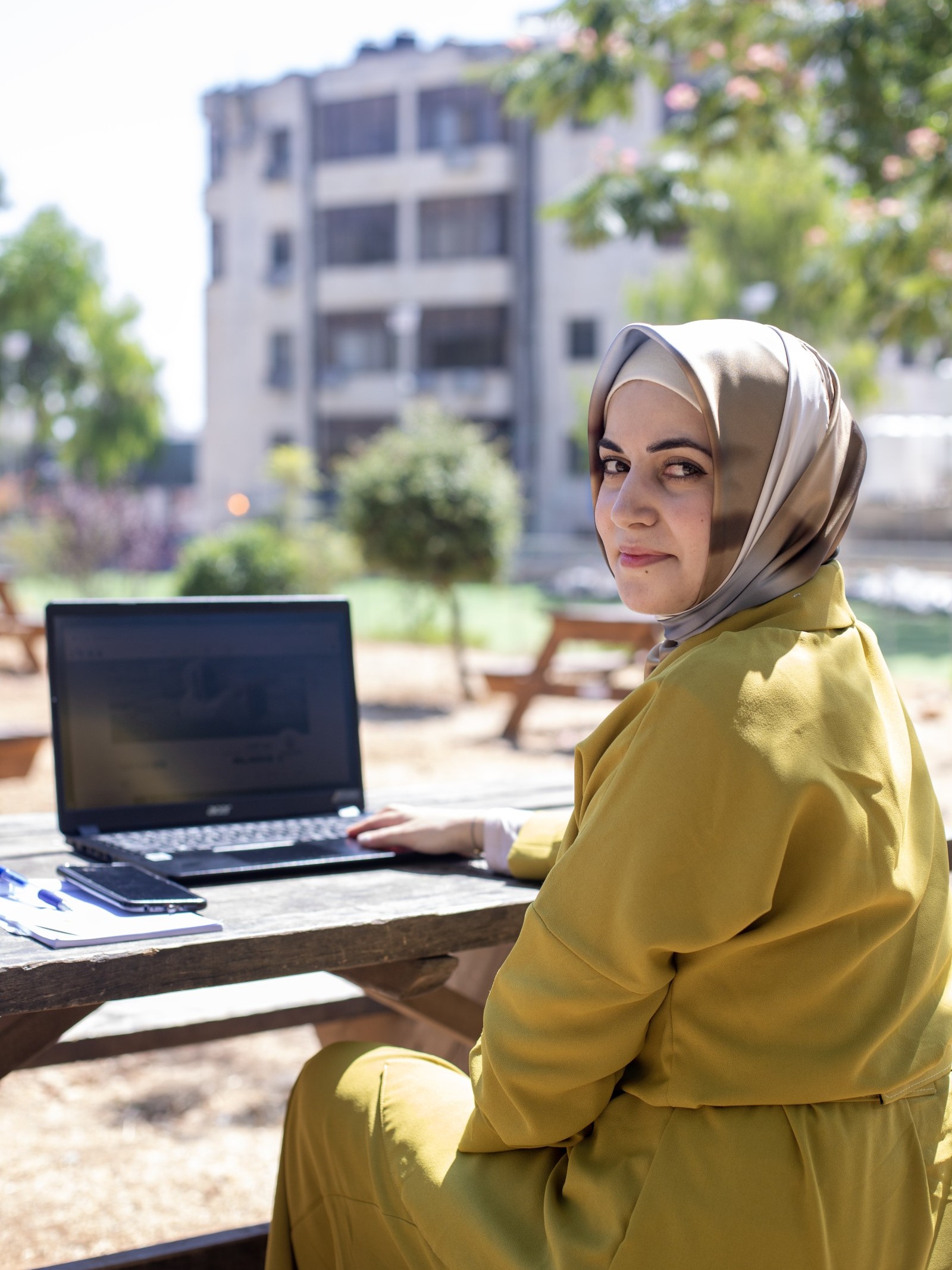 Junge Frau mit Kopftuch aus Palästina sitzt draussen an einem Laptop