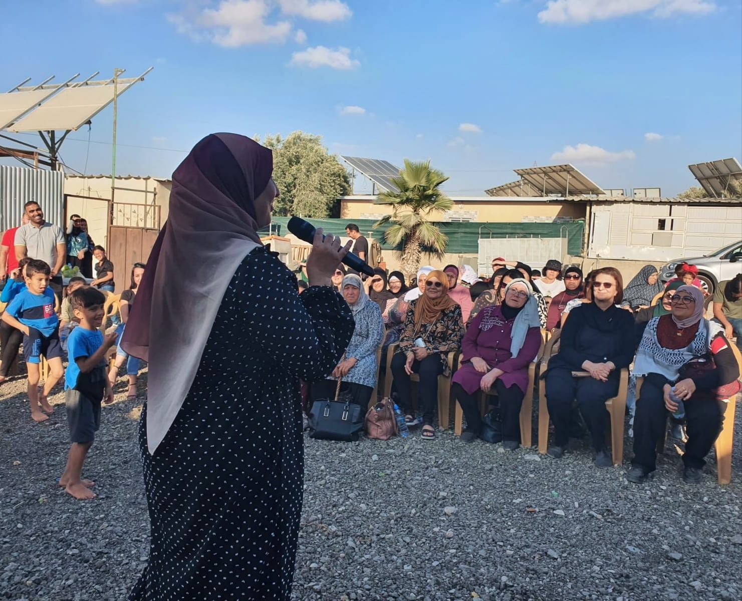 Frau mit Kopftuch in Israel spricht durch ein Mikrofon zu einer Gruppe von sitzenden Frauen