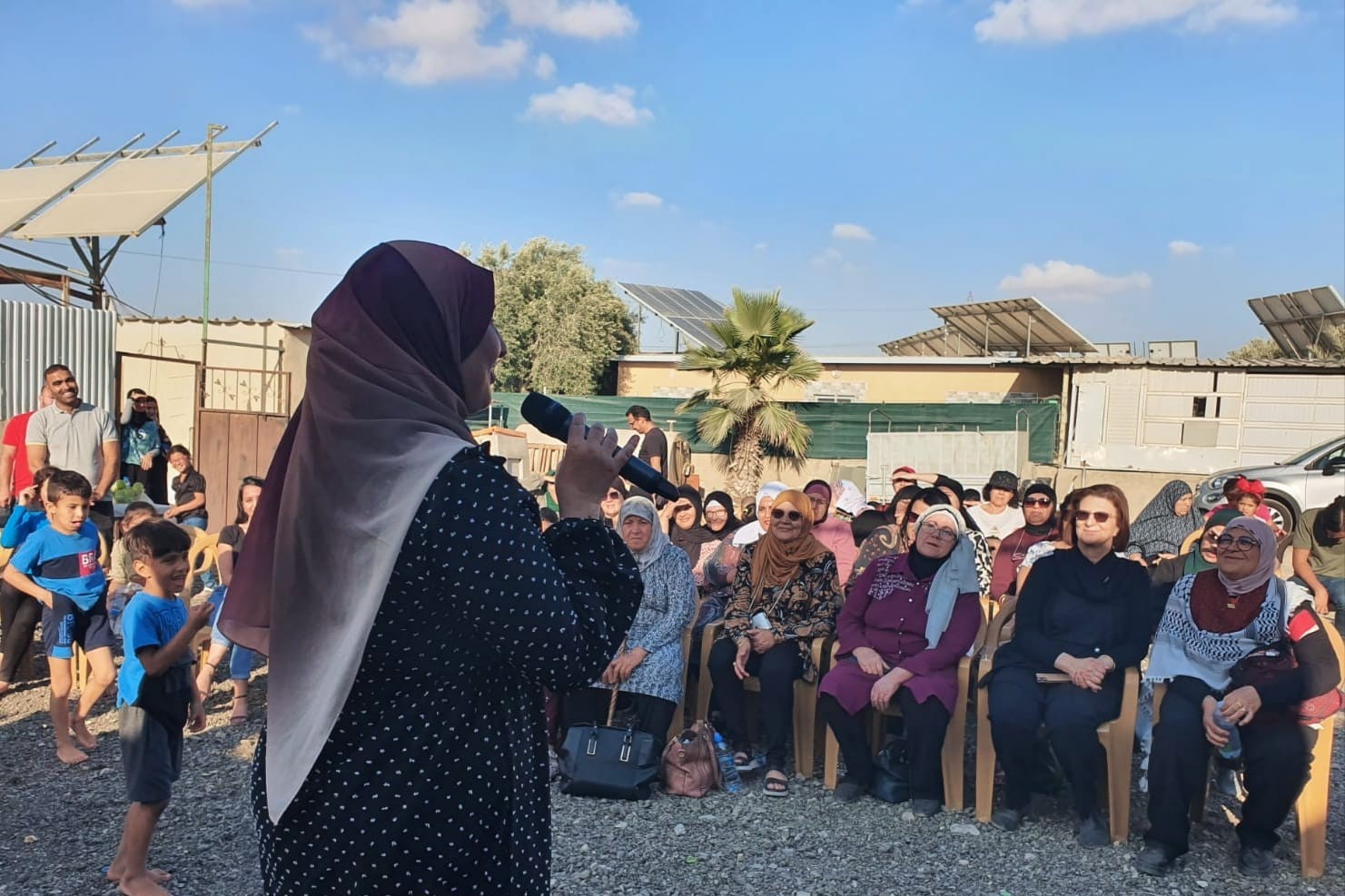 Frau mit Kopftuch in Israel spricht durch ein Mikrofon zu einer Gruppe von sitzenden Frauen